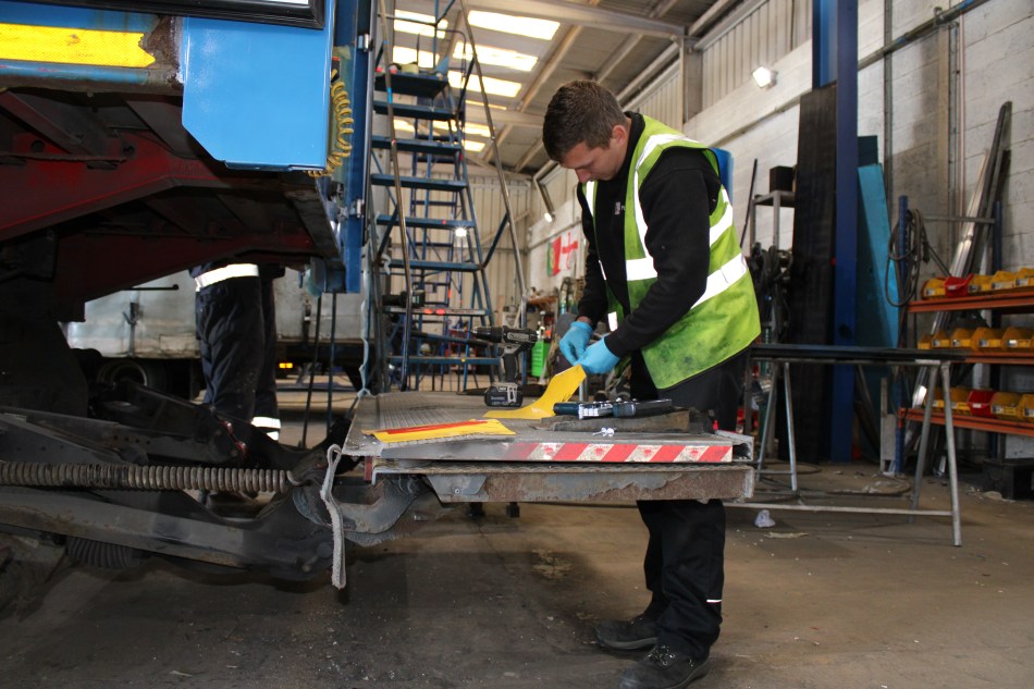 Engineer inspecting and repairing a commercial vehicle tail lift in a workshop